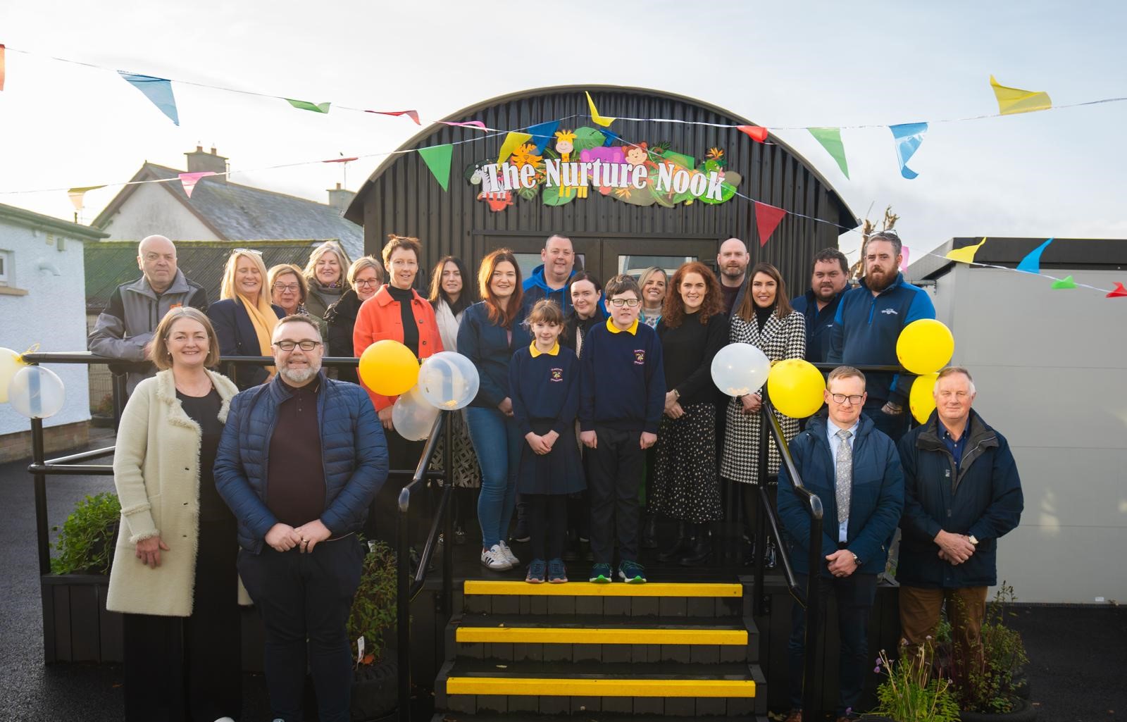 Members of the School Community stand in front of the building with a sign which says 'Nurture Nook' on the front.